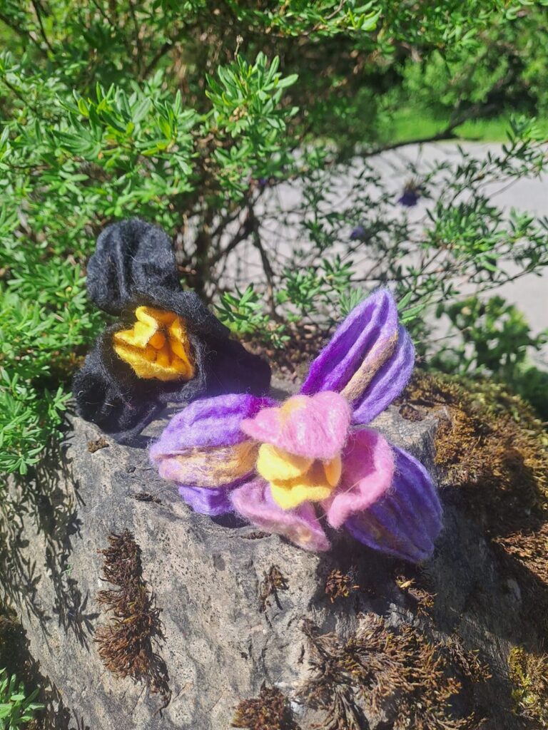 Gefilzte Blüten in Lila und Gelb auf einem Stein im Garten