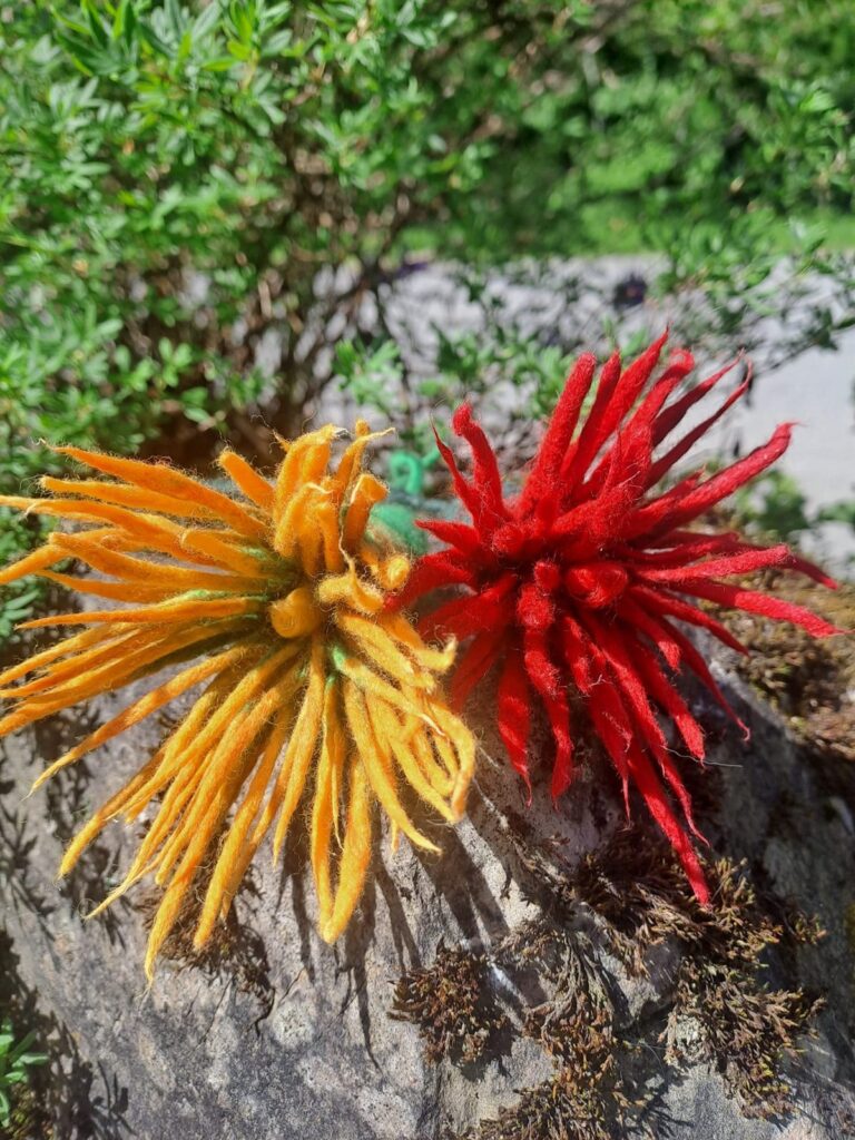 Zwei gefilzte Blüten in Orange und Rot auf einem bemoosten Baumstrunk