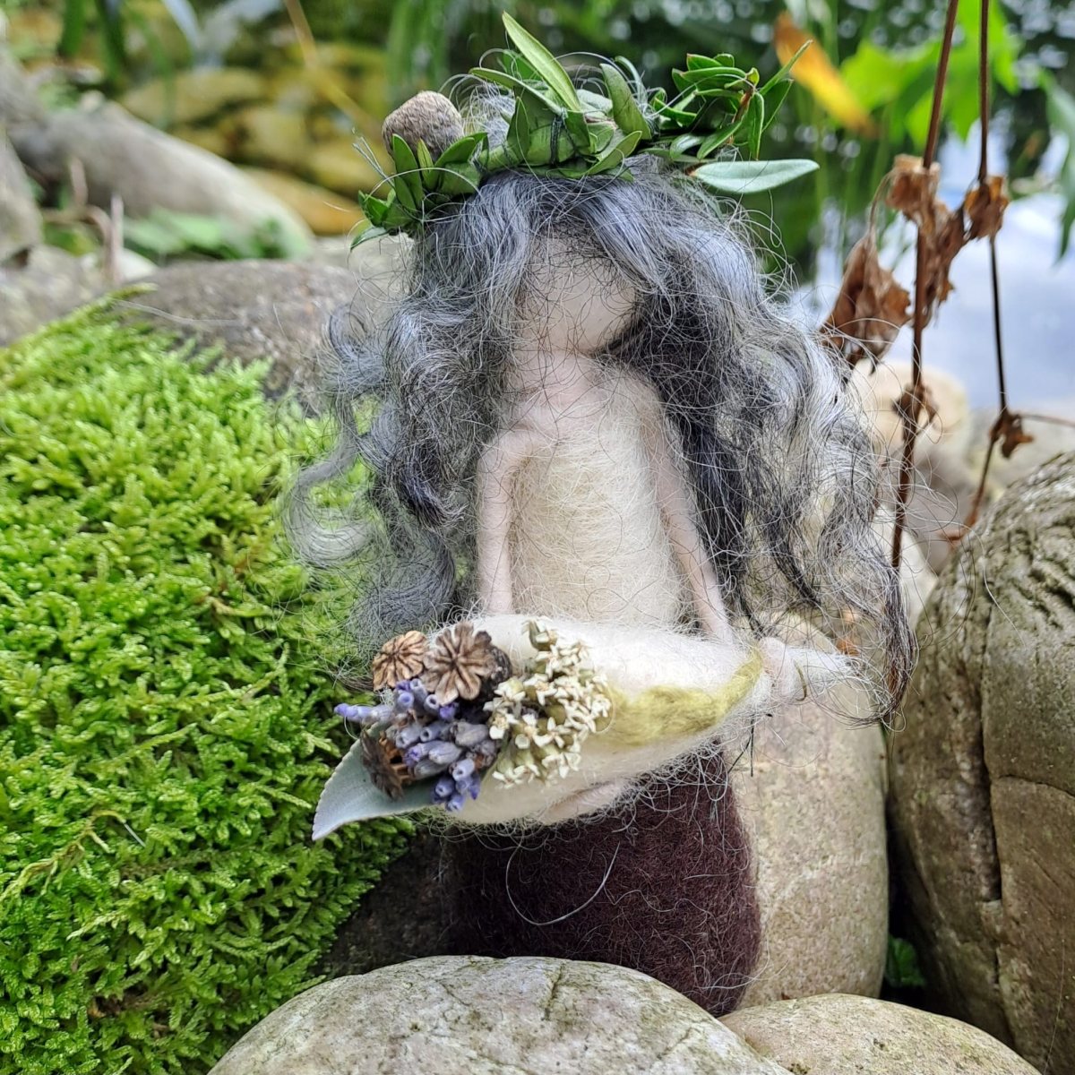 Gefilzte Figur mit Blätterkranz hält ein Blatt mit getrockneten Blüten, daneben leuchtend grünes Moos