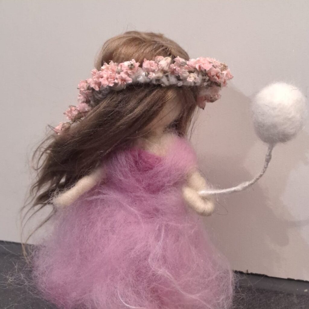 Gefilzte Figur eines Mädchens mit langem Haar, rosa Blumenkranz und rosa Kleid, das einen weissen Ballon hält