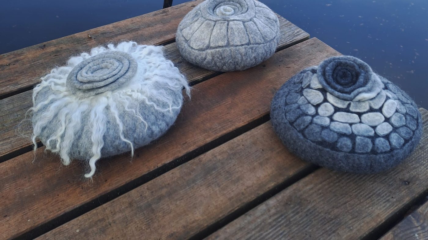 Drei verschieden gemusterte gefilzte Urnen auf einem Holzsteg am See mit Schilf