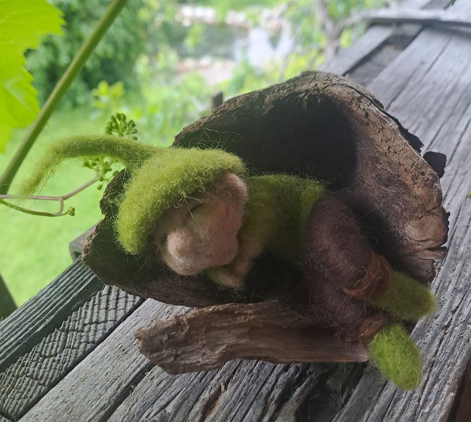 Schlafendes gefilztes Waldkind in Grün, eingebettet in ein Stück Rinde